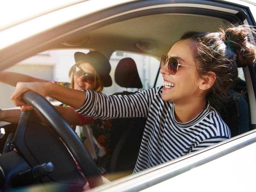 Women driving a car with a friend in the passenger seat and windows down