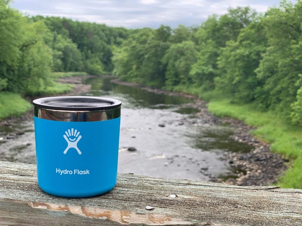Travel mug resting on a wooden surface overlooking a river.