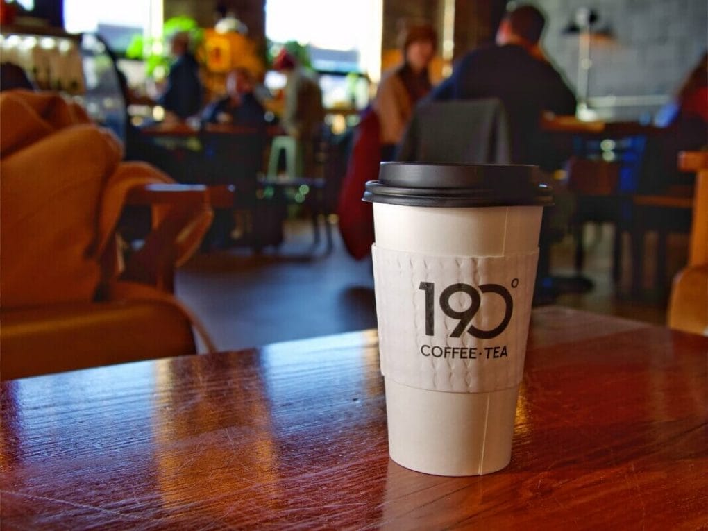 Coffee cup with 190-degree Coffee & Tea logo on a wood table in a coffee shop in Duluth.