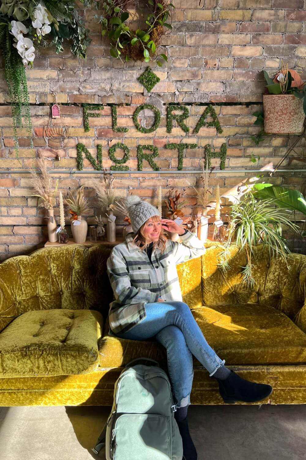 Me sitting on a green coach in front of a brick wall with Flora North spelled out in plants.