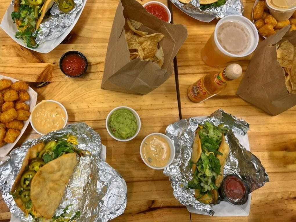 A table filled with plates of tacos, salsa, tortilla chips and beer.