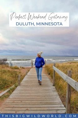 Text: Perfect Weekend Getaway Duluth Minnesota Image: Me walking on a boardwalk in front of Lake Superior with a winter hat on.