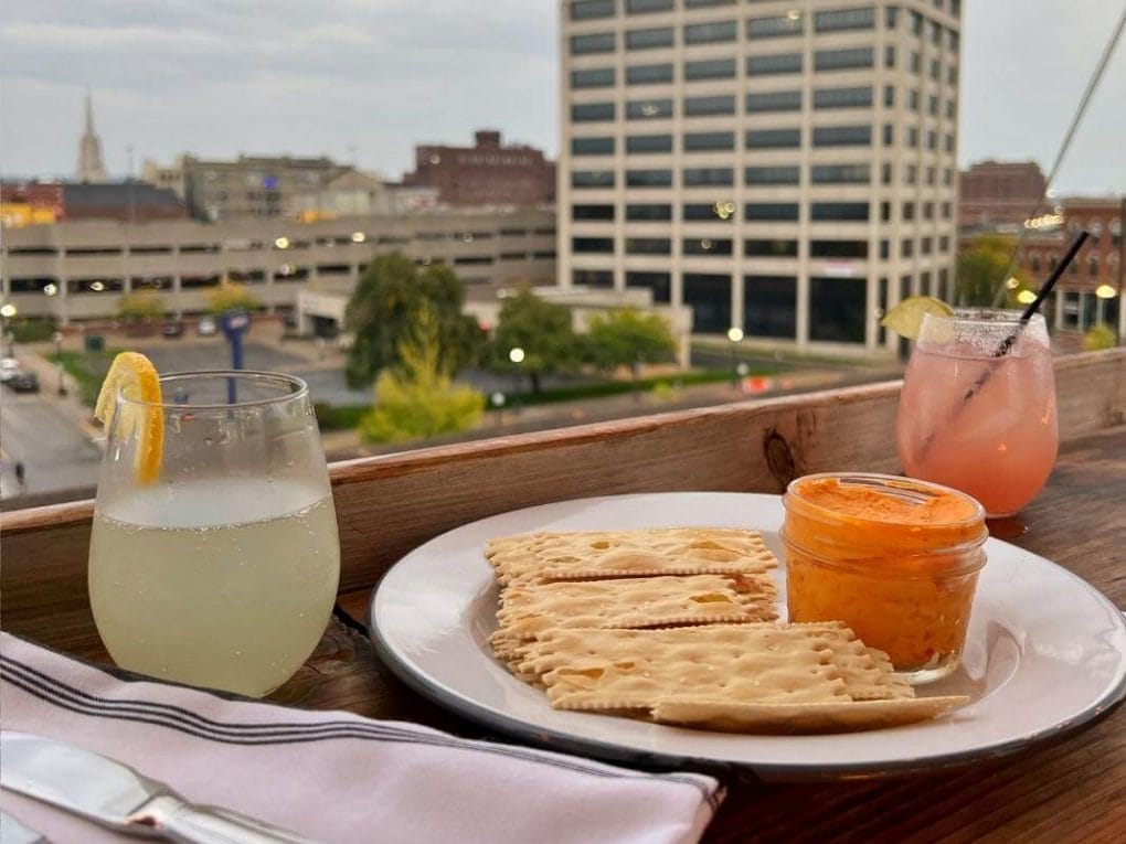 Cocktails and a plate with pimento cheese and crackers with a view from the rooftop of The Charmant Hotel.