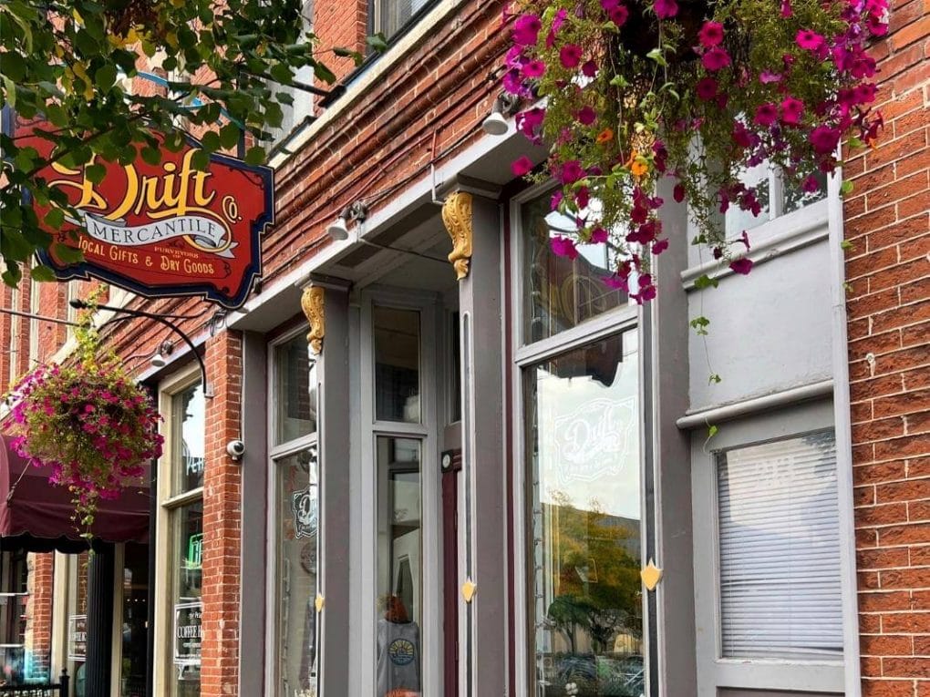 Exterior of Drift Mercantile is a brick building with hanging flower pots and large display windows.