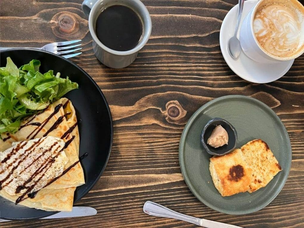 Overview photo of a savory crepe, coffee, latte and homemade biscuit on a wooden table.